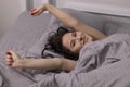 Happy sleepy girl brunette in burgundy top under grey sheets in bed. morning routine. good dream, sleeping Royalty Free Stock Photo