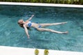 Happy slender young woman lies on a water surface in the pool and has a rest