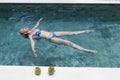 The happy slender young woman lies on a water surface in the pool and has a rest