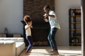 Happy small african american kid dancing with dad in living room.