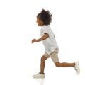 Happy small black boy in shorts and shirt is running. Side view. Full length, isolated