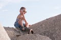 Happy small boy in sunglasses and vest sits on a breakwater