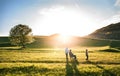 A small girl with her senior grandparents with wheelchair on a walk outside in sunset nature.