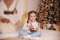 Happy small girl holding traditional Christmas striped candy cane on lights background at home. Smiling Little girl sitting on bed Royalty Free Stock Photo