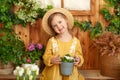 Happy small girl plants flowers in a pot on porch of house. Little girl in straw hat and dress with potted flowers in spring garde