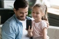 Happy small girl showing funny mobile application to smiling daddy.