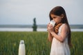 Happy small girl in a white dress drinking milk in a green field