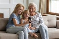 Multi-generational women family sit on sofa using smartphone Royalty Free Stock Photo