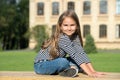 Happy small kid with long hair in casual fashion style sit on park bench relaxing on sunny summer day outdoors, leisure