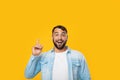 Happy smart adult caucasian man with beard raises finger up at copy space