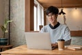 A happy and smart Asian male college student is using his laptop while sitting in a coffee shop Royalty Free Stock Photo