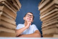 Happy smart boy in glasses sitting between two piles of books and look up smiling Royalty Free Stock Photo