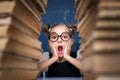 Happy smart girl in rounded glasses sitting between two piles of books and look at camera surprised Royalty Free Stock Photo