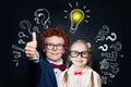 Happy smart little girl and boy student with lightbulb on blackboard background. Brainstorming and idea concept