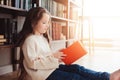 Happy smart schoolgirl reading books in library or at home