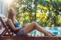 Happy smartphone woman relaxing near swimming pool listening with earbuds to streaming music. Beautiful girl using her Royalty Free Stock Photo