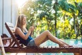 Happy smartphone woman relaxing near swimming pool listening with earbuds to streaming music. Beautiful girl using her Royalty Free Stock Photo