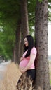 Happy smile Asian Chinese pregnant woman in yoga dress lean on tree in forest nature outdoor enjoy peaceful time live relaxed life Royalty Free Stock Photo