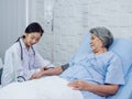 Happy smile Asian elderly old female patient in light blue dress lying on bed while beautiful young woman doctor. Royalty Free Stock Photo