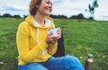 Happy smile girl holding in hands cup of hot tea on green grass in outdoors nature park, beautiful woman hipster enjoy drinking Royalty Free Stock Photo