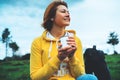 Happy smile girl holding in hands cup of hot tea on green grass in outdoors nature park, beautiful young woman hipster enjoy drink Royalty Free Stock Photo