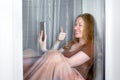 Happy smile girl sits on windowsill by window and holding smartphone.