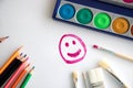 Happy smile painted with raspberry paint on a white sheet of paper with colored pencils, a box with paint and brushes for painting Royalty Free Stock Photo