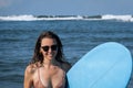 Happy smile young brunette woman hold blue surfboard going out of ocean after morning surfing. Portrait of beautiful girl spending Royalty Free Stock Photo