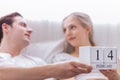 Happy smile young caucasian couple or lover in bed together. Man and woman hold 14 February calendar on Valentine day as anniversa Royalty Free Stock Photo