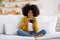 Happy african american little girl sitting on couch with smartphone Royalty Free Stock Photo