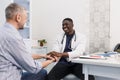 A happy smiling African-American male doctor supports the patient during the consultation, sitting at the table Royalty Free Stock Photo