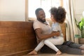 Happy smiling african american man sitting on floor, holding daughter.