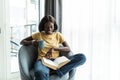 Happy smiling african american woman drink coffee sitting on sofa and reading book at home Royalty Free Stock Photo