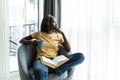 Happy smiling african american woman drink coffee sitting on sofa and reading book at home Royalty Free Stock Photo