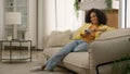 Happy smiling African American woman ethnic girl on comfortable sofa cozy couch chatting online use mobile app scrolling Royalty Free Stock Photo