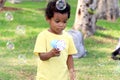 Happy smiling African boy with black curly hair making soap bubbles with blowing bubble gun toy at green garden. Kid spending time Royalty Free Stock Photo