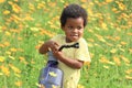 Happy smiling African boy with black curly hair watering yellow orange cosmos flower garden. Kid spending time outdoors in Royalty Free Stock Photo