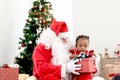 Happy smiling African child girl baby sitting on Santa Claus lap with decorative Christmas tree as background, cute kid open Royalty Free Stock Photo