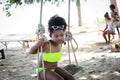 Happy smiling African girl with black curly hair wearing brightly colored swimsuit, sitting on swing at beach outdoor, beautiful Royalty Free Stock Photo