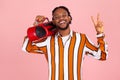 Happy smiling african man with beard and dreadlocks in striped shirt showing v sign with fingers holding red tape recorder on Royalty Free Stock Photo