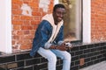 Happy smiling african man sitting with vintage film camera on city street over brick wall Royalty Free Stock Photo