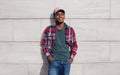 Happy smiling african man wearing red plaid shirt, baseball cap posing on city street, gray brick wall