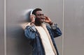 Happy smiling african man in wireless headphones listening to music on city street over gray metal wall Royalty Free Stock Photo