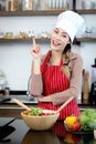 Happy smiling Asian beautiful woman with hand gesture pointing up wearing apron chef hat at kitchen. Cute young female chef Royalty Free Stock Photo