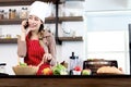 Happy smiling Asian beautiful woman wear apron and chef hat, talking on mobile phone during prepare fresh vegetables salad at Royalty Free Stock Photo