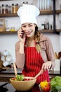 Happy smiling Asian beautiful woman wear apron and chef hat, talking on mobile phone during prepare fresh vegetables salad at Royalty Free Stock Photo