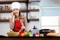 Happy smiling Asian beautiful woman wear apron and chef hat, talking on mobile phone during prepare fresh vegetables salad at Royalty Free Stock Photo
