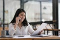 Happy smiling asian business woman working on laptop at office, using smart phone. Businesswoman sitting at her working Royalty Free Stock Photo