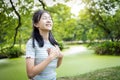 Happy smiling asian child girl standing in green nature,holding hands on heart,female teenage touching her chest,enjoy breathing