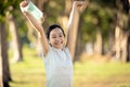 Happy smiling asian child girl is standing with raised arms up,holding mask in her hand in green nature,woman enjoy breathing Royalty Free Stock Photo